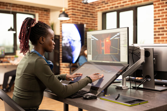 African american woman seated with multi screens, brainstorming digital design ideas at a creative agency. Young black female designer reviewing 3D concepts on her desktop monitor. - Powered by Adobe