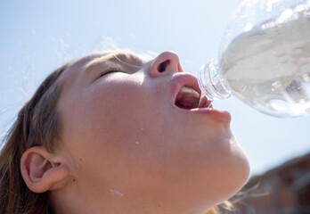 Young boy enjoying fresh water from a bottle, revitalizing herself under the bright summer sun,...
