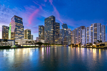 The vibrant skyline of the Brickell neighborhood in Miami, with illuminated buildings and palm trees under a colorful twilight sky.