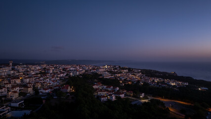 City lights creating a magical glow over Nazare, Portugal, as dusk settles, viewed from a high vantage point