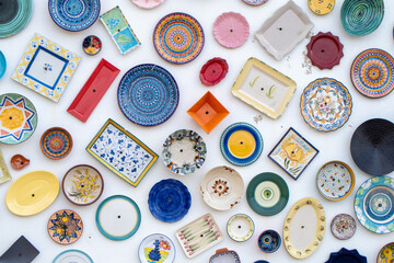 Variety of colorful ceramic plates and dishes with different shapes and patterns hanging on a white...