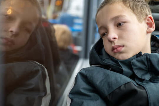 Portrait of a sad pensive boy traveling by bus and looking out the window during a cold winter day