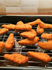 A rack of chicken goujons are on a metal cooking tray. The nuggets are golden brown and crispy. Simple tasty family meal. Cooking meat. concept