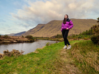 Teenager girl enjoys stunning nature scenery with mountain, brown wild grass fields and river...
