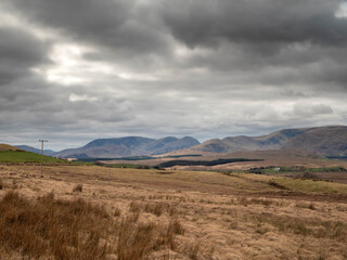 Huge field with brown grass and mountains in the background, dark, dramatic sky. Nature scene in...