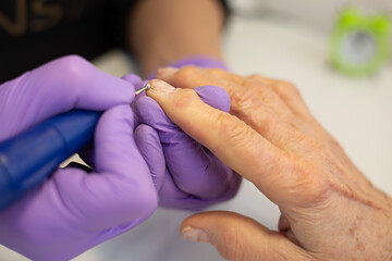 A beautician uses a modern professional electric manicure and pedicure machine to file an elderly woman's nails. Various steps to achieve a perfect and simple manicure in a beauty salon. A modern