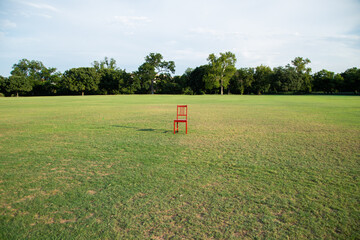 A single red chair stands in the middle of a wide grassy field under a clear sky. Symbolic and...