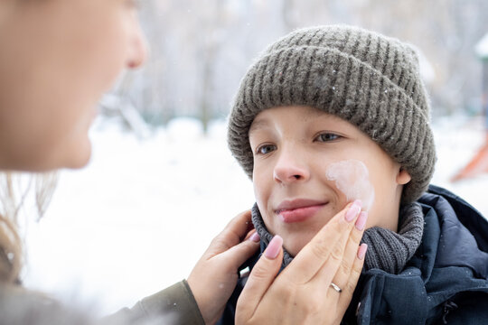Caring mother applying protective sunscreen or moisturizing cream on her son's face during wintertime outdoor activities - Powered by Adobe