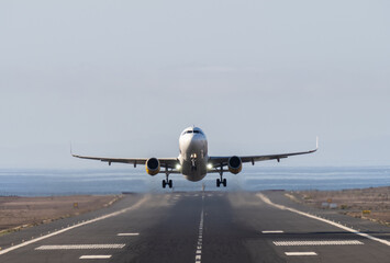 Front view of a white passenger airplane taking off from a runway next to the sea under a clear sky © danr13