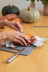 Female preparing sweet potato on cutting board with squash in background