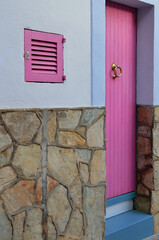 Pink wooden door and window shutter on a stone and plaster wall