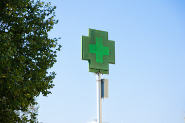 Green pharmacy cross sign on a pole against blue sky in Portugal