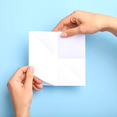 Hands meticulously fold a sheet of white paper, creating a simple origami design against a light blue background.
