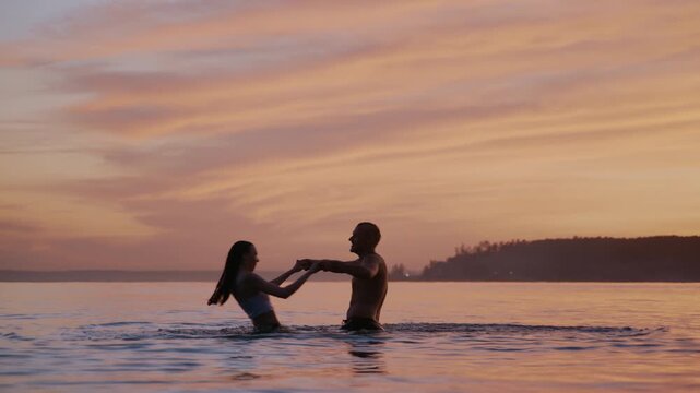 Romantic couple playing and holding hands in the ocean at sunset