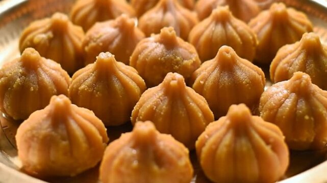 Close up of a golden plate filled with many delicious looking modak sweets arranged neatly together