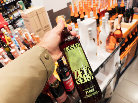 Frankfurt, Germany - Dec 30, 2024: A hand holding a Ziegler Zeitgeist Flora aperitif bottle in a vibrant liquor store section, surrounded by colorful bottles of wine, champagne, and other beverages.