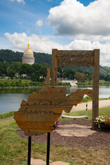 A view of the state capital building in Charleston, West Virginia, USA from across the Kanawha River. Signage in the shape of the state reads, "Almost Heaven."