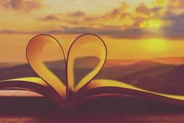 Open bible book with heart shape at sunset