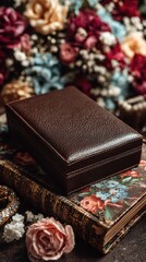 Brown leather box resting on a floral book surrounded by colorful dried flowers and rings