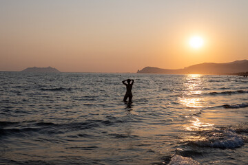 Silhouettes of swimming people on sunset in sun lights, sandy beach near Sperlonga, Lazio, italy,...