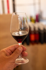 Hand with glass of Banyuls AOC aged natural sweet grand cru Banyuls fortified dessert wine from vines from slopes Pyrenees in Roussillon, France made in glass jar Dame Jeanne, demijohn