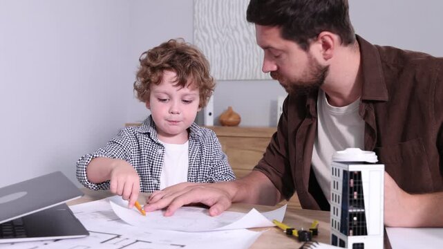 Choice of profession. Father and his son exploring engineering drawings at table indoors, camera moving in