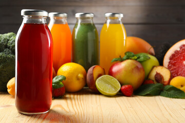 Tasty juices in glass bottles, fresh ingredients and herbs on wooden table against brown background, closeup