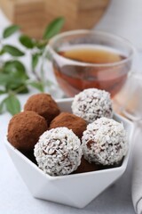 Delicious homemade candies with cocoa powder and coconut flakes in bowl on white table, closeup