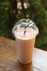 Tasty milkshake in plastic cup on wooden table outdoors