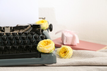 Vintage typewriter with roses, notebook and gift box on cloth near white wall