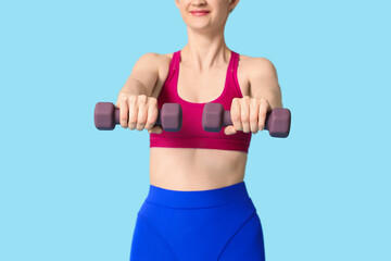 Sporty young woman with dumbbells on blue background