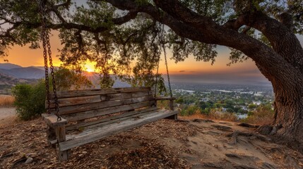 Fototapeta premium A rustic swing hangs gracefully from a majestic tree, offering a serene view of a stunning sunset over a distant town