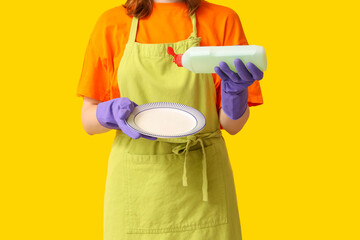 Young woman pouring dish soap onto plate on yellow background, closeup