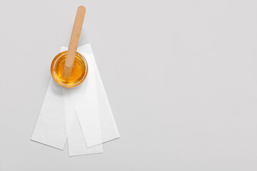 Glass bowl with sugaring paste, wax strips and wooden stick on grey background