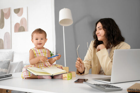Working mother and her little baby with notebook on table at home