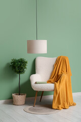 Hanging lamp, decorative tree and armchair with plaid near green wall in room