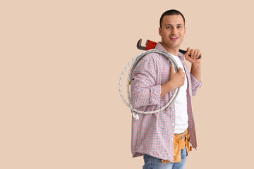 Male plumber with wrench and hose on beige background