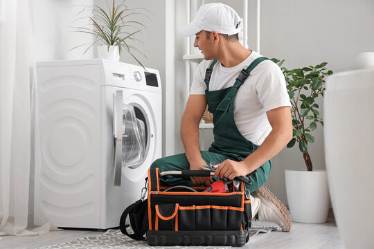 Male plumber with bag of tools fixing washing machine in bathroom