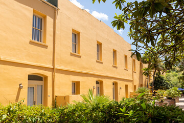 Charleston, South Carolina, USA - July 2, 2025: A yellow stucco residential building with multiple windows and lush greenery in the foreground under a bright summer sky.