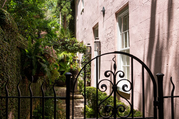 Obraz premium Wrought iron gate opens to a lush courtyard beside a pink stucco home in historic Charleston, South Carolina,
