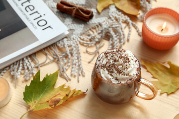 Autumn composition with cup of cocoa, leaves and burning candle on wooden background, closeup