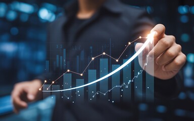 A businessman's hand uses a glowing digital pen to draw a rising arrow on a virtual bar graph, symbolizing business growth, strategic planning, and successful financial investment