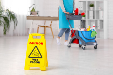 Janitor with trolley and caution sign in office