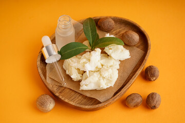 Wooden plate with shea butter, nuts and essential oil on color background