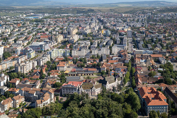 high-angle view of Deva, a city in Hunedoara County, Romania, showing a blend of old and new architecture, with lush green trees and a scenic backdrop