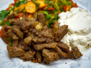 A delicious and traditional Turkish meal of beef saute or kavurma served with a fresh vegetable salad and a side of creamy yogurt on a white plate representing local cuisine