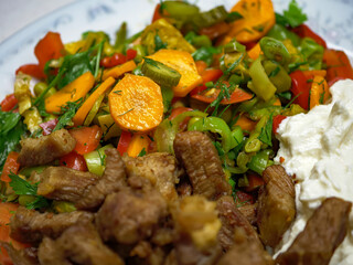A close-up of a homemade Turkish dish featuring cooked beef cubes fresh salad with carrots and peppers and a dollop of yogurt a hearty and nutritious meal