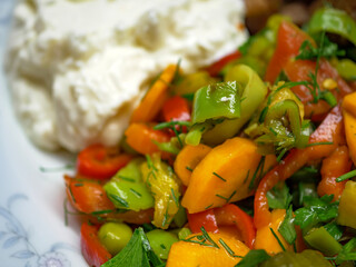 A side view of a fresh vegetable salad next to a dollop of creamy white yogurt this image...