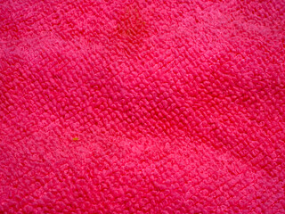 A macro photograph of a pink or red terrycloth towel showing the woven loops and fibers of the...