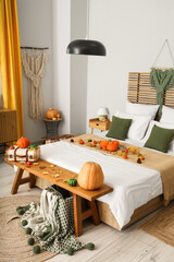 Bed with autumn decor and bench with suitcase and pumpkins in interior of  bedroom